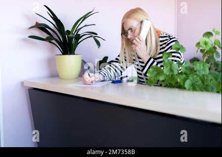 Attraktive Frau mittleren Alters spricht am Arbeitsplatz am Telefon Stockfoto
