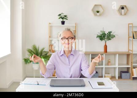 Friedliche, zufriedene Geschäftsfrau, die meditiert, während sie am Arbeitsplatz im Büro sitzt. Stockfoto