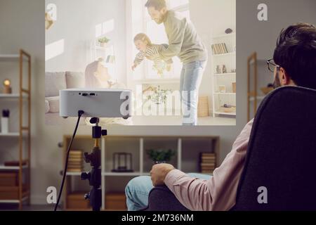 Junger Mann, der zu Hause einen Film oder Familienfotos auf einem modernen Projektor ansieht Stockfoto