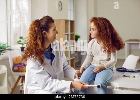 Eine Ärztin tippt das kleine Mädchen mit einem Spezialhammer auf das Knie, um ihre Reflexe zu überprüfen. Stockfoto