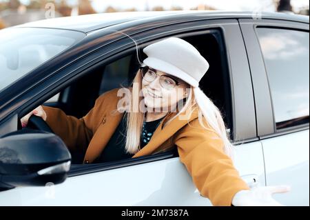 Aufgeregte, flirtende Frau mittleren Alters, die das Lenkrad hält und ein Auto fährt Stockfoto