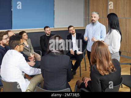 Professioneller männlicher Leiter und Coach, der Mitarbeiter ausbildet, spricht bei Treffen mit verschiedenen Managern. Stockfoto