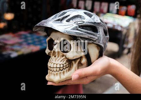 Unbekannte Touristin, die beim Besuch des Straßenmarkts einen künstlichen menschlichen Schädel mit einem Fahrradhelm zeigte Stockfoto