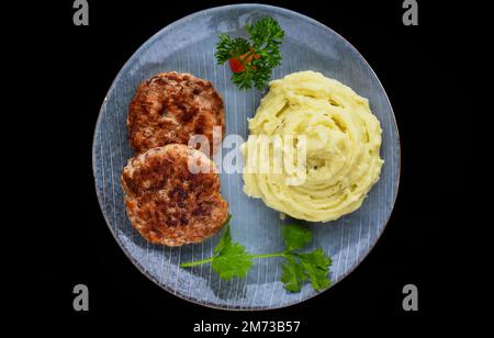 Kartoffelpüree mit Fleischschnitzeln auf schwarzem Hintergrund, Draufsicht Stockfoto
