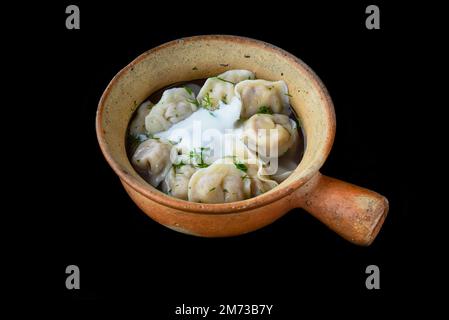 Russische Knödel Pelmeni mit saurer Sahne auf schwarzem Hintergrund, Seitenansicht Stockfoto