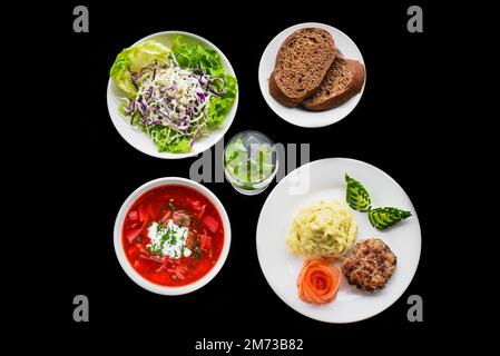 Kombi-Set mit Borschtsch, Kartoffelpüree, schwarzem Brot, Salat auf schwarzem Hintergrund, Draufsicht Stockfoto