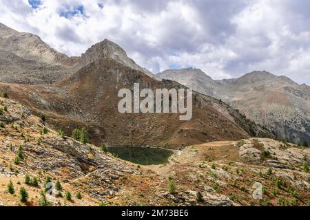 Kleiner alpiner Loie-See (Lago di Loie), umgeben von Felsen mit seltenen Zwergbäumen und gelblichem Moos unter schweren weißen Wolken im Parco Nazionale Stockfoto