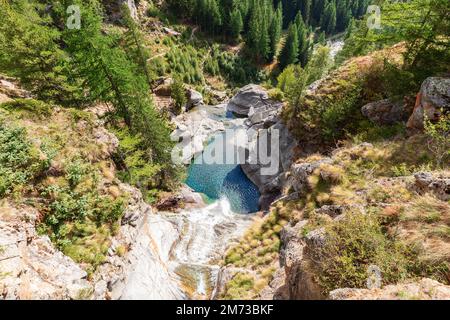 Blick von oben auf den Lillaz-Wasserfall (Cascate di Lillaz) und den smaragdgrünen Teich darunter, Felsen mit grün-gelber Herbstvegetation und Kiefern Stockfoto