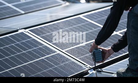 Männliche Teamingenieure, die eigenständige Solarpaneele installieren. Elektriker montieren blaues Solarmodul auf dem Dach des Unternehmens. Alternati Stockfoto