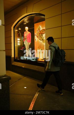 Ein junger Mann kommt nachts an einem ETRO-Schaufenster vorbei, das hell beleuchtet ist. Moskau, Russland. Stockfoto