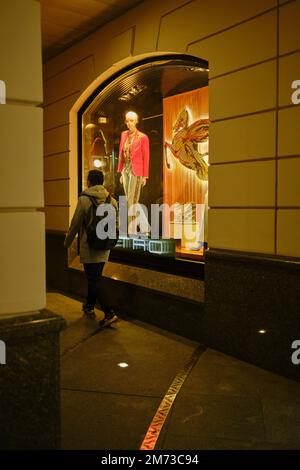 Ein junger Mann kommt an einem Schaufenster vorbei, das nachts hell beleuchtet ist. Moskau, Russland. Stockfoto