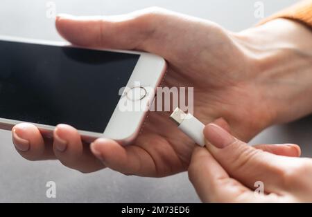 Smartphone wird auf weißem Hintergrund per Hand aufgeladen. Blick von oben. Laden Sie Ihr Telefon auf. Stockfoto