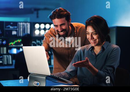 Glückliches Geschäftspaar, das im Büro an einem Laptop arbeitet. Junge Handelsteams, die lächelnd Daten auf dem pc-Bildschirm ansehen. Zwei Partner arbeiten im Finanzbereich zusammen. Hochwertiges Foto Stockfoto