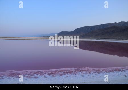 Die Bergkette spiegelt sich im Abendlicht im rosafarbenen Wasser des pinkfarbenen Sees Shiraz, Iran, wider Stockfoto