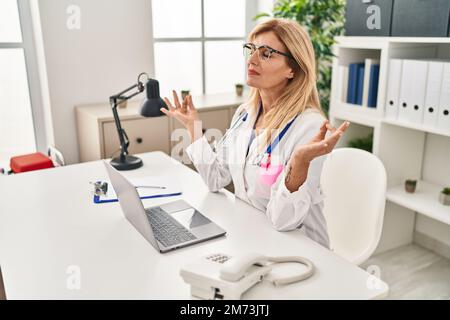 Blonde Frau mittleren Alters in der Ärzteinform, die in der Klinik Yoga-Übungen macht Stockfoto