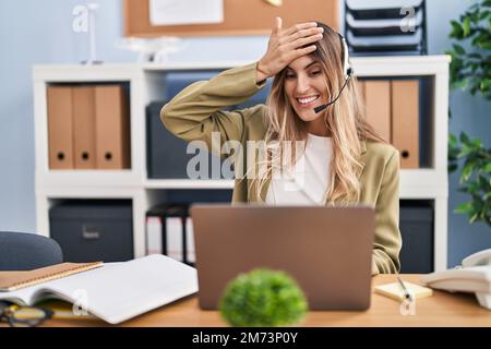 Junge hispanische Frau mit Headset für Callcenter-Agenten, die im Büro arbeitet, gestresst und frustriert von Hand an Kopf, überrascht und wütend Stockfoto