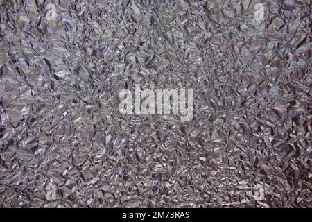 Zerknitterter Hintergrund aus Aluminiumfolie. Glänzendes und getöntes facettiertes, zerknittertes Material. Stockfoto