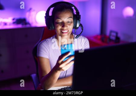 Junge schöne hispanische Frau streamer mit Computer und Smartphone im Spielzimmer Stockfoto