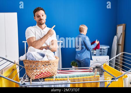 Hispanische Mutter und Sohn hängen Kleider an der Wäscheleine auf und lächeln fröhlich mit Hand und Finger zur Seite Stockfoto