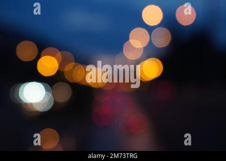 Bokeh abstrakter Hintergrund von unscharfem Stadtverkehr mit Autolampen und Straßenlaternen bei Nacht. Helle Farbpunkte auf dunkelmarineblauem Hintergrund. Stockfoto