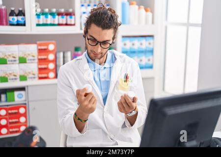 Junger hispanic-Mann Apotheker hält Pillen Flaschen in der Apotheke Stockfoto