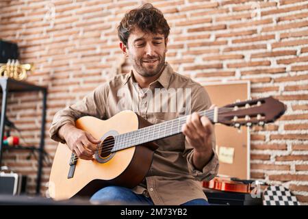 Junger Musiker, der im Musikstudio lächelnd und selbstbewusst klassische Gitarre spielt Stockfoto