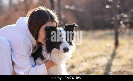 Eine weiße Frau umarmt ihre Hundegrenze Collie, während sie im Herbstpark auf einer Bank sitzt. Stockfoto