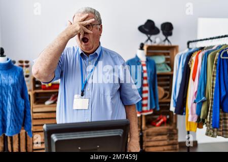 Älterer Mann mit grauen Haaren, der als Manager in einer Boutique arbeitet, der in einen Schock schaut, Gesicht und Augen mit der Hand verdeckt, durch Finger mit Embarr schaut Stockfoto