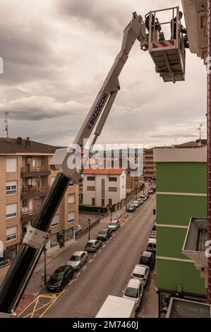 Arbeiter auf einem Kran mit Hebekorb repariert die Wand des Gebäudes. Der Baumeister in der hydraulischen Hebebühne reinigt die Dachrinne der Fassade. Stockfoto