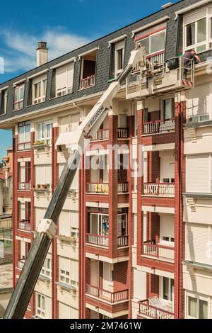 Arbeiter auf einem Kran mit Hebekorb repariert die Wand des Gebäudes. Der Baumeister in der hydraulischen Hebebühne reinigt die Dachrinne der Fassade. Stockfoto