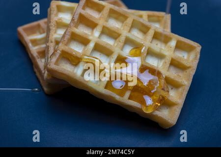 Waffeln auf blauem Teller, während sie mit Honig garniert werden Stockfoto