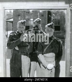 England. 1940er Jahre Drei Soldaten der britischen Armee, die bei den Royal Engineers arbeiten, posieren für ein Selbstporträt, das durch Fotografieren in einen Spiegel geschaut wird. Während des Zweiten Weltkriegs tragen die Männer Kampfkleidung und Seitenkappen. Ein Soldat, ein Lanze-Korporal, raucht eine Pfeife, während ein anderer mit einer Klappkamera fotografiert. Ein ungewöhnliches Selfie der 1940er Jahre! Stockfoto