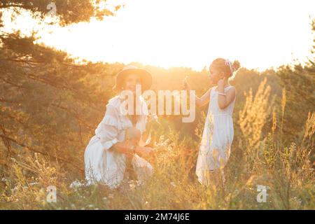 Charmante, lächelnde Frau, Mutter in der Hocke und kleines blondes Mädchen, Tochter im Kleid, die Spaß in der Natur hat Stockfoto