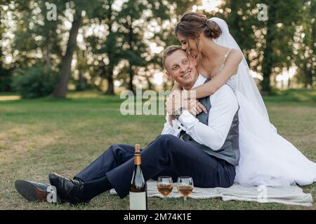 Vertikales frisch verheiratetes Brautpaar im Hochzeitskleid, küsst den Bräutigam, umarmt und trinkt Champagner am Hochzeitstag Stockfoto