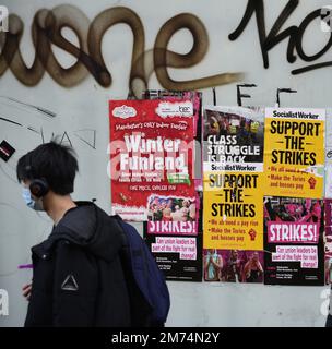 Manchester, Vereinigtes Königreich, 7. Januar 2023. Ein Mann geht an Plakaten vorbei, die hauptsächlich von Socialist Worker produziert wurden, an einem leeren Schaufenster in Manchester, Großbritannien, die Passanten drängen, die Streiks zu unterstützen. Kredit: Terry Waller/Alamy Live News Stockfoto