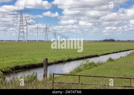 Holländische Landschaft in Groningen mit Windturbinen und Strommasten Stockfoto