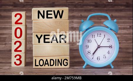 2023 Neujahr Text auf Holzblöcken und Holzhintergrund mit Uhr laden. Zielvereinbarung und Neujahrsvorsätze. Weihnachts-Upload. Stockfoto