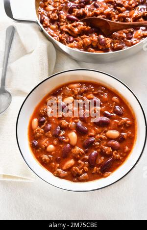 Cowboybohnen mit Rinderhack, Jalapeno-Pfeffer und Speck in der Schüssel auf weißem Steinhintergrund. Stockfoto