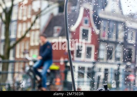 Stadtbild - Blick auf die alten Häuser von Amsterdam und Radfahrer im Regen durch die Windschutzscheibe des Motorrads, Niederlande Stockfoto