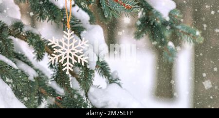 Süße Dekoration in Form einer hölzernen Schneeflocke auf einem Weihnachtsbaum, draußen neben dem Haus, Nahaufnahme Stockfoto