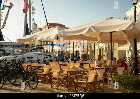 Leute frühstücken in einem Café, umgeben von festgemachten Yachten in Gaios, Paxos, Ionischen Inseln, griechischen Inseln, Griechenland Stockfoto