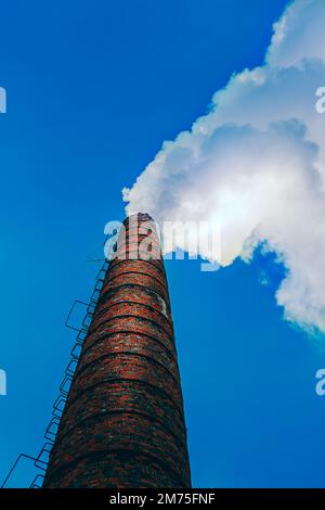 Ein alter roter Ziegelkamin am Himmel, aus dem Rauch kommt Stockfoto