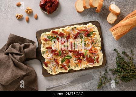 Beliebtes Butterboard mit Zwiebeln, Knoblauch, Orange, Kräutern, knusprigem Baguette und Toast auf grauem Hintergrund. Blick von oben. Stockfoto