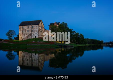 Das beleuchtete mittelalterliche Schloss Kastelholm und seine Spiegelungen an einem ruhigen Fluss auf den finnischen Åland-Inseln bei Abenddämmerung im Sommer. Stockfoto