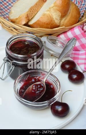 Kirschmarmelade in einer kleinen Schüssel mit Löffel, schwarze Kirschen Stockfoto