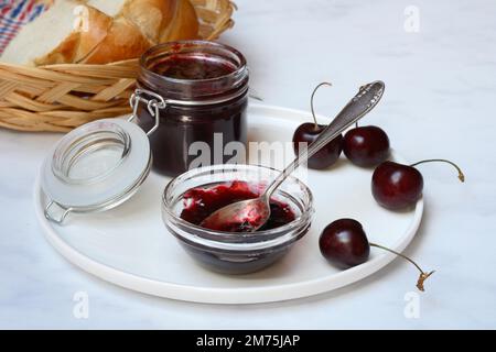 Kirschmarmelade in einer kleinen Schüssel mit Löffel, schwarze Kirschen Stockfoto