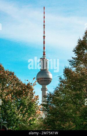 Die Abbildung zeigt den Berliner Fernsehturm aus großer Entfernung. Auf der linken und rechten Seite bilden zwei Bäume einen Vordergrund, während sich der Fernseher in der Mitte befindet. Stockfoto