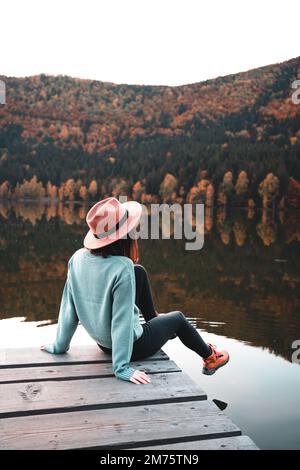 Seitenansicht einer modischen jungen Frau, die auf einem Holzdock sitzt Stockfoto