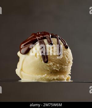 Vanille-Eiskugel mit geschmolzener Schokolade auf dunkelgrauem Hintergrund Stockfoto