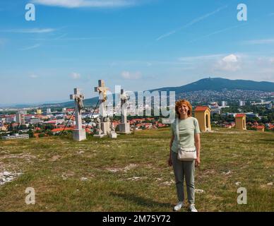 Eine reife Frau mittleren Alters mit blonden Haaren steht vor einer Aussichtsplattform auf dem Berg Calvaria in der Stadt Nitra in der Slowakei. Stockfoto